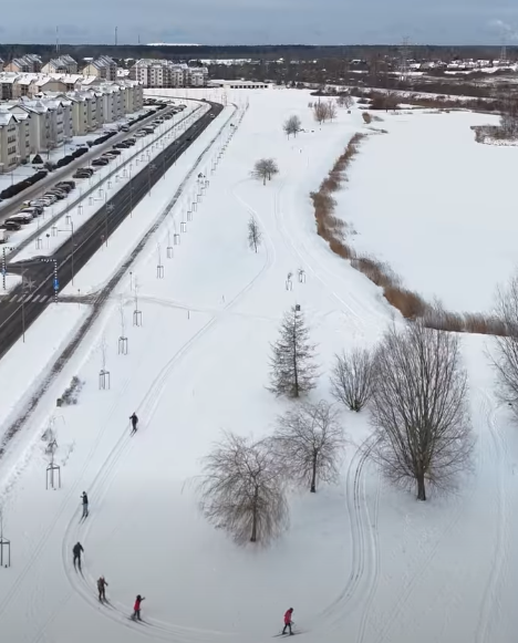 Cilvēki slēpo sniegotā parkā pie dzīvojamām ēkām un aizsaluša dīķa Salaspilī, Nometņu ielā.