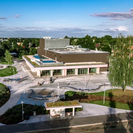 Jaunās Salaspils koncertzāles ēka ar zaļu jumtu un plašu priekšlaukumu ar soliņiem un strīklaku, kas aicina atpūsties.