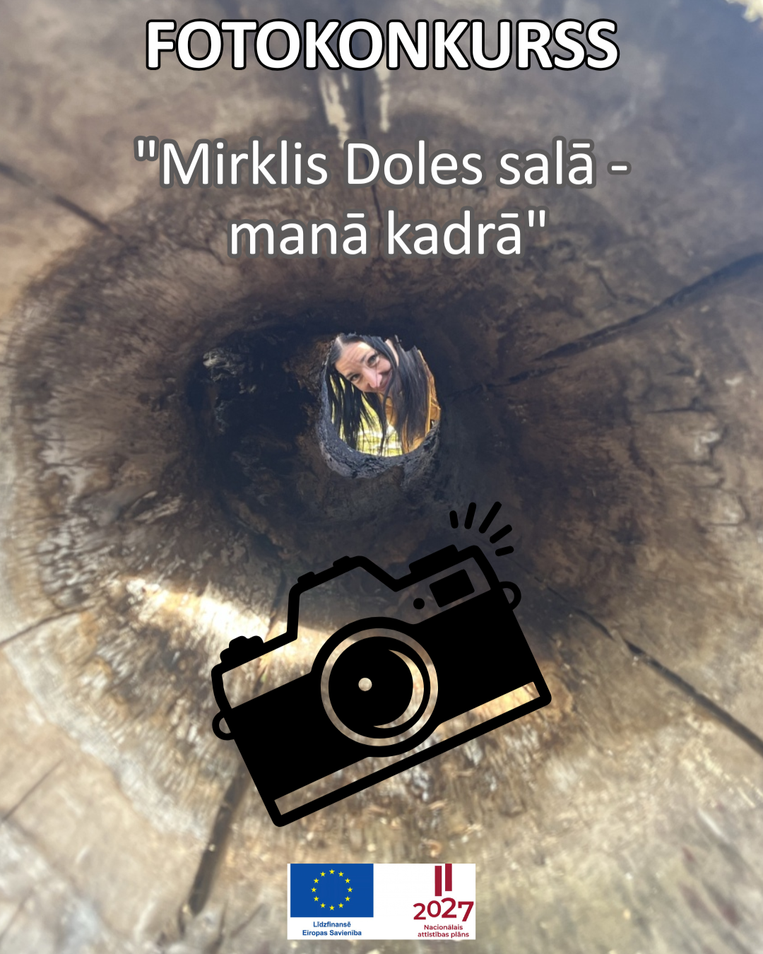 FOTOKONKURSS "Mirklis Doles salā – manā kadrā". Koka stumbra dobums, caur kura atvērumu redzama smaidoša seja, simbolizējot fotoattēlu uzņemšanu dabā. Uz attēla redzams fotoaparāta simbols.