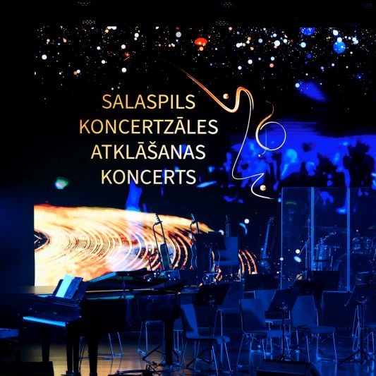 Koncertzāles skatuve ar klavierēm, mūzikas instrumentiem, krēsliem un lielu ekrānu, kas rāda uzrakstu "SALASPILS KONCERTZĀLES ATKLĀŠANAS KONCERTS".